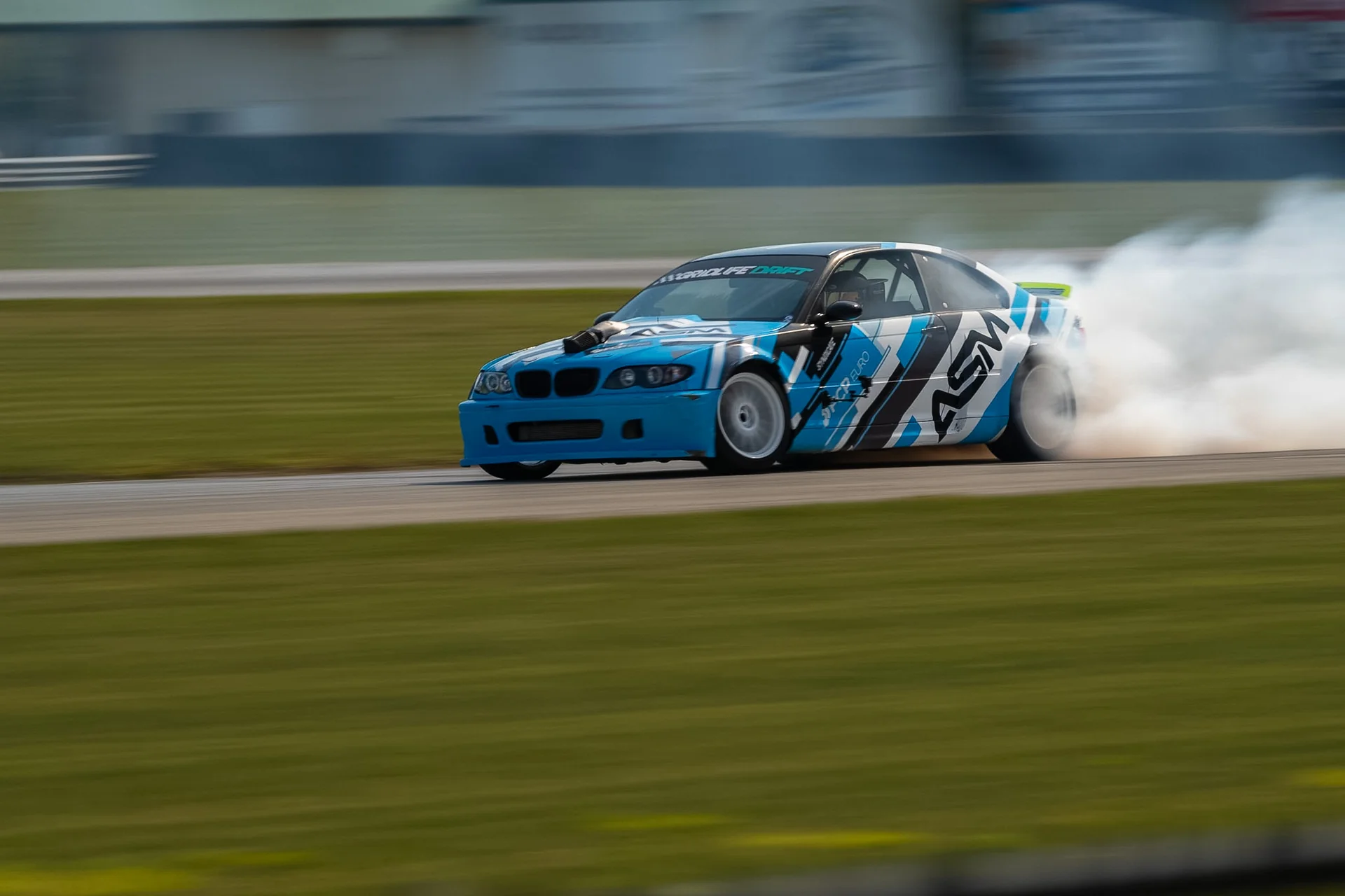 Blue and white drift car trailing tire smoke on track