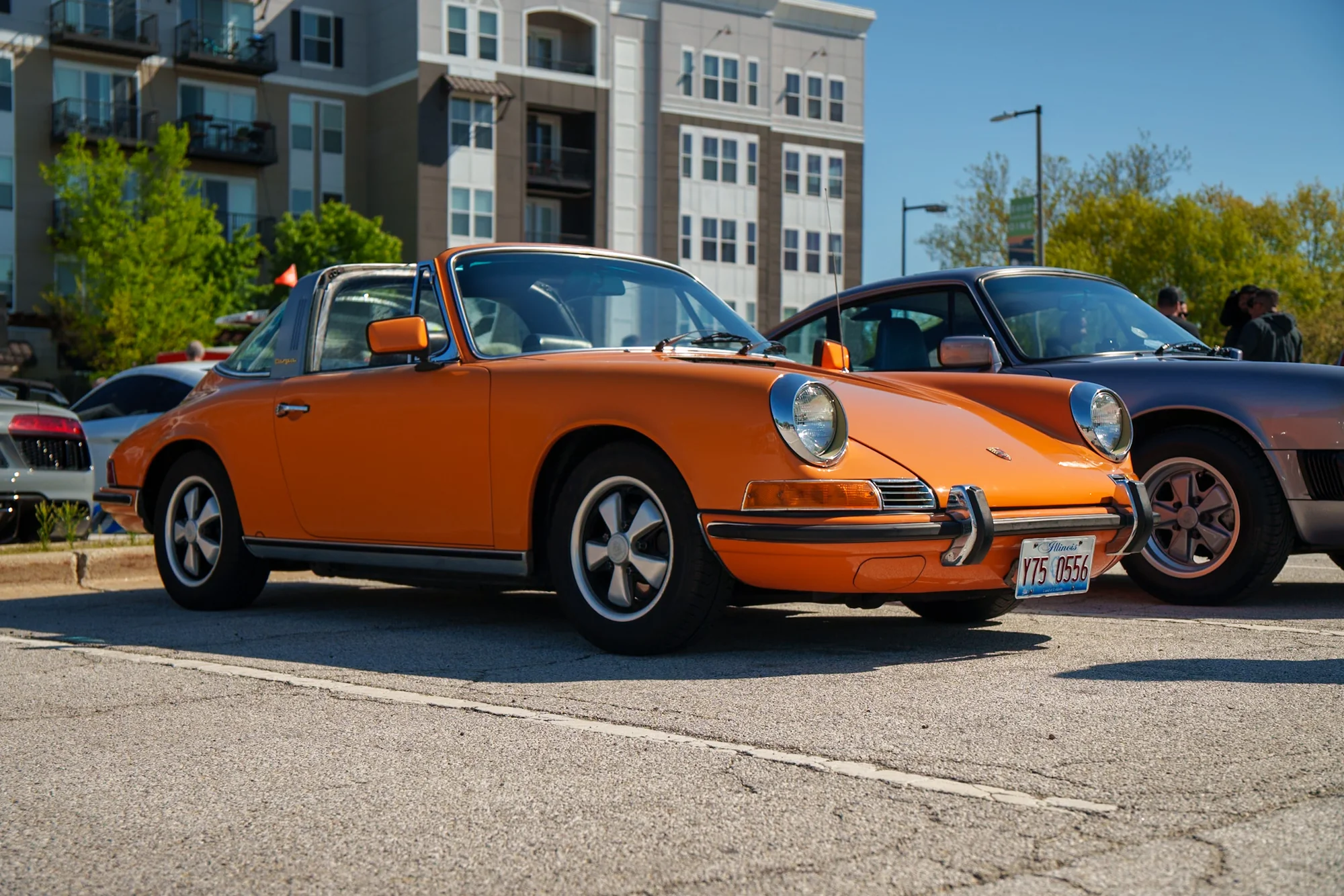 An orange classic Porsche parked beside a modern city building