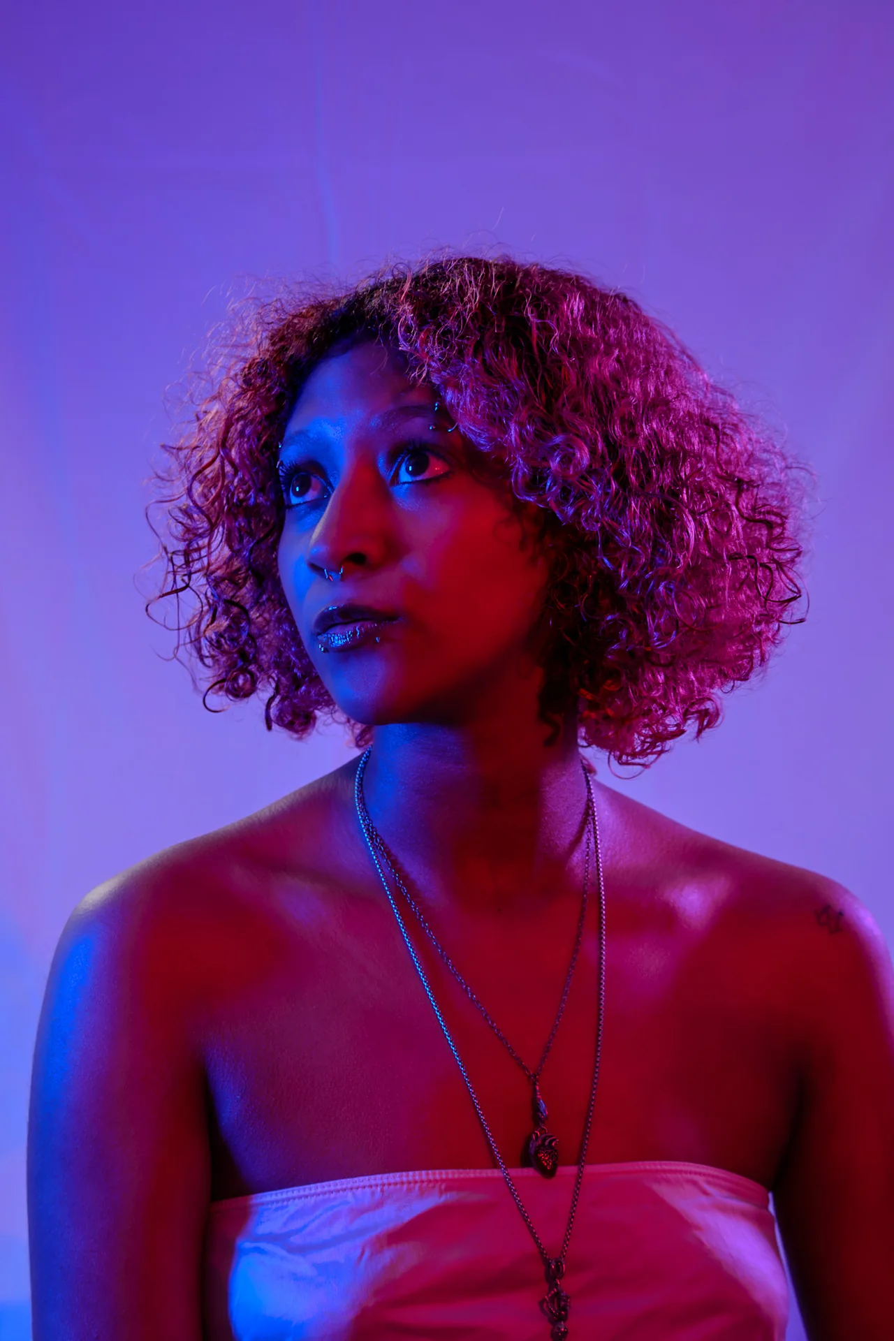 Person with curly hair photographed in contrasting violet and red studio light